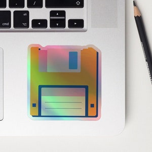 May include: A holographic sticker of a floppy disk. The disk is yellow with a blue tab and a blue window. The sticker has a rainbow iridescent effect.