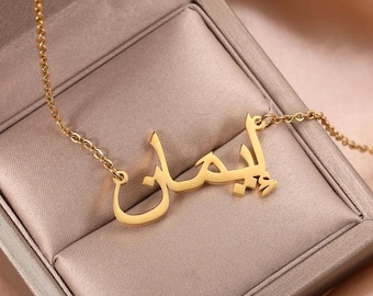 May include: A gold necklace with a nameplate pendant featuring the Arabic word "أحلام" in a delicate, cursive script.