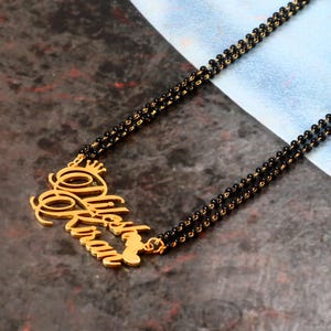 May include: Gold necklace with a black beaded chain and a pendant featuring the names "Nilesh" and "Kiran" in a cursive script.