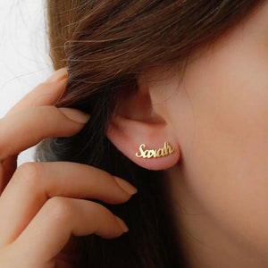 Peut inclure: Boucles d'oreilles dorées avec le nom "Sarah" écrit en cursive.