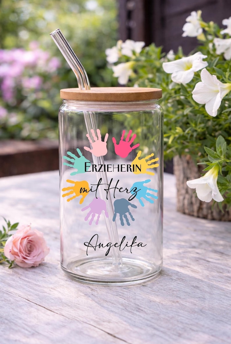 May include: A clear glass tumbler with a bamboo lid and a glass straw. The tumbler is decorated with colorful handprints and the text "ERZIEHERIN mit Herz Angelika".