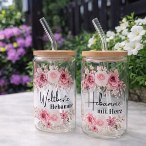 May include: Two clear glass tumblers with bamboo lids and bent glass straws. Each glass features a floral design with pink roses and green leaves. The left glass displays the text Weltbeste Hebamme, and the right glass displays Hebamme mit Herz.