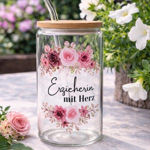 Op de afbeelding: Een doorzichtig glazen beker met een bamboe deksel en een glazen rietje, voorzien van een bloemmotief met roze en bordeauxrode rozen en bladeren. De tekst "Erzieherin mit Herz" staat in zwarte schrijf- en schreefletters in het midden.