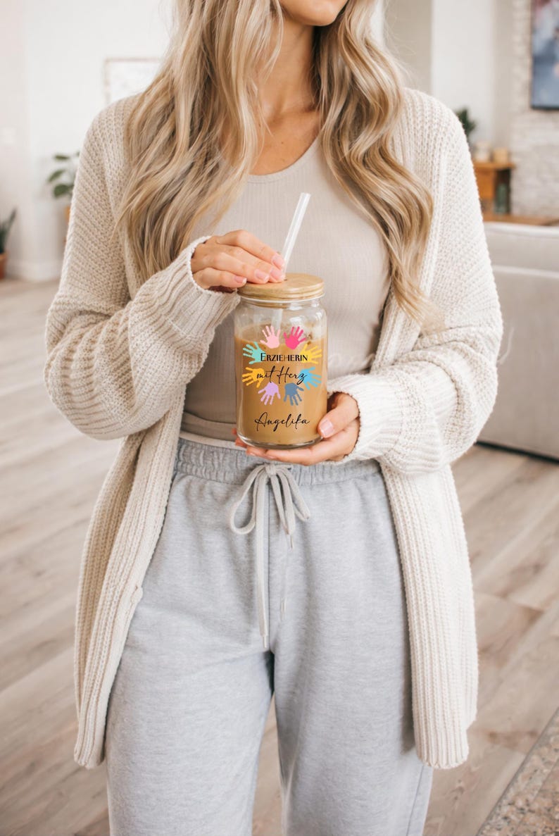 May include: A clear glass tumbler with a wooden lid and a straw, filled with a light brown beverage. The tumbler is decorated with colorful handprints and text that reads "Erzieherin mit Herz Angelina."