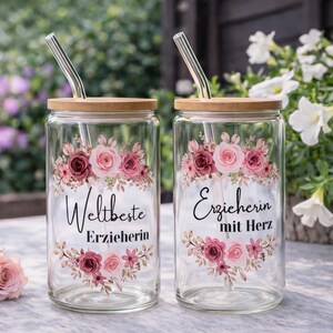 Op de afbeelding: Twee doorzichtige glazen met bamboe deksels en metalen rietjes. Elk glas heeft een bloemmotief in roze en bordeauxrode tinten. Op het linkerglas staat "Weltbeste Erzieherin" en op het rechterglas "Erzieherin mit Herz" in zwarte letters.