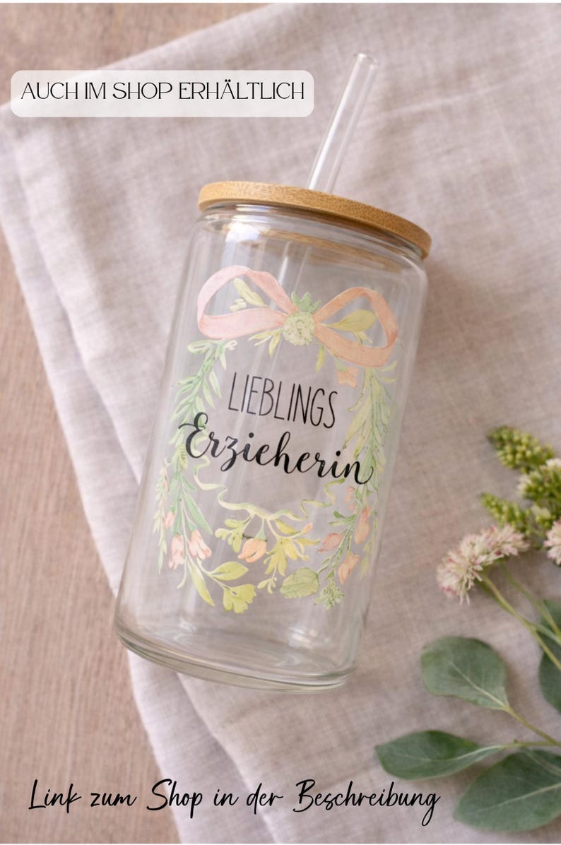 May include: A clear glass tumbler with a bamboo lid and a glass straw. The glass features a watercolor-style floral wreath design in soft pink and green tones, surrounding the black printed text "LIEBLINGS Erzieherin" in a mix of fonts.