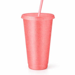 Puede incluir: Un vaso reutilizable de color coral con tapa a juego y una pajita recta. La taza presenta un acabado de superficie texturizado y ligeramente moteado en todo el exterior, proporcionando una apariencia mate consistente desde la base hasta el borde.