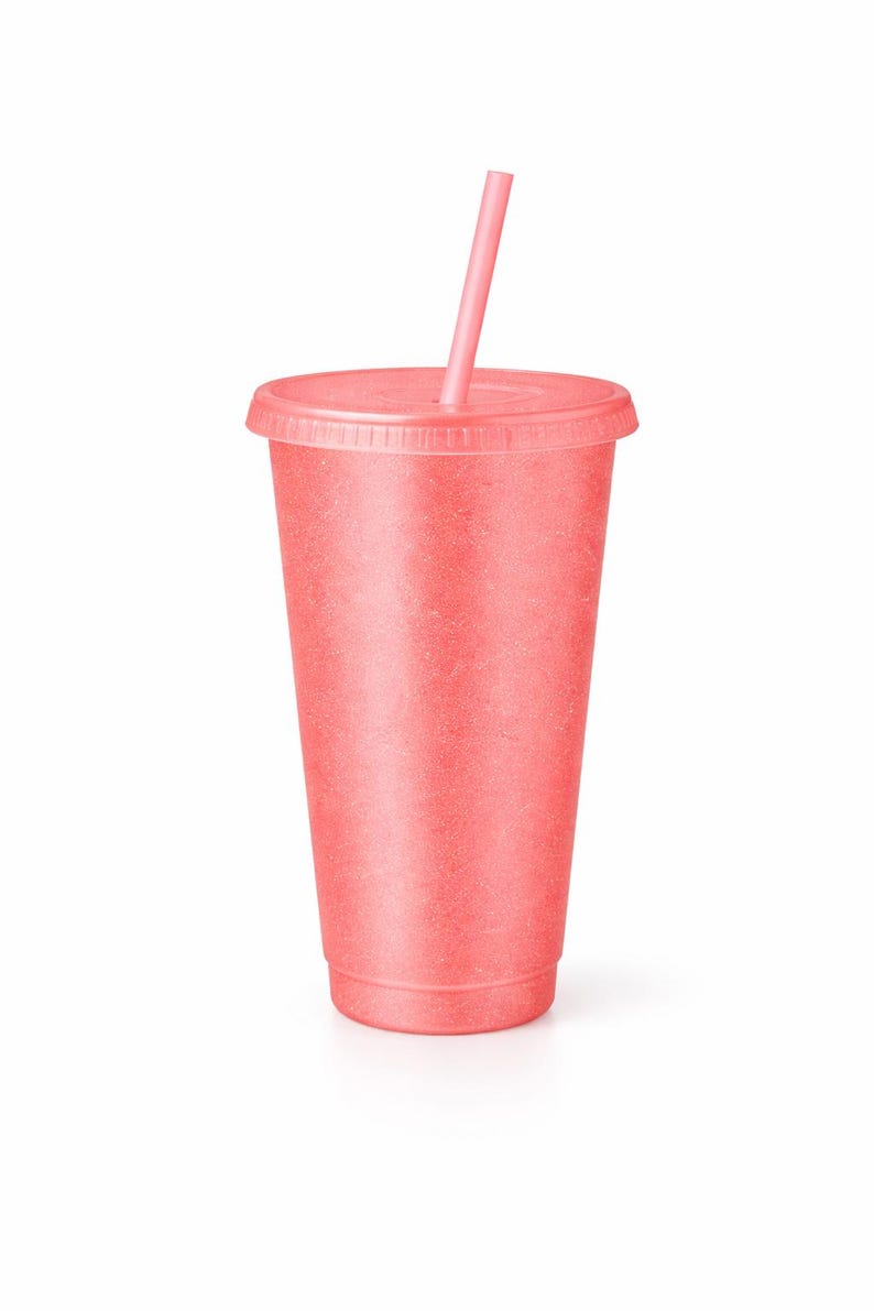Puede incluir: Un vaso reutilizable de color coral con tapa a juego y una pajita recta. La taza presenta un acabado de superficie texturizado y ligeramente moteado en todo el exterior, proporcionando una apariencia mate consistente desde la base hasta el borde.