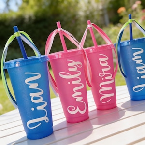Puede incluir: Cuatro vasos de pl&aacute;stico con tapa y pajita, dos azules y dos rosas, cada uno con un nombre en letra blanca: Liam, Emily, Mira y Liam. Cada pajita est&aacute; decorada con cintas de colores atadas en la parte superior, creando un aspecto festivo.