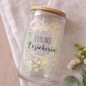 May include: A clear glass tumbler with a wooden lid and a straw. The tumbler features a floral design with the words "LIEBLINGS Erzieherin" and the text "Auch im Shop erh&auml;ltlich" and "Link zum Shop in der Beschreibung".