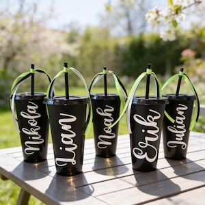 Puede incluir: Cinco vasos de pl&aacute;stico negro mate con tapas y pajitas negras, cada uno personalizado con un nombre en letra blanca: Nikola, Lian, Noah, Erik y Julian. Cada pajita est&aacute; decorada con una cinta de color verde lima y blanco atada arriba.