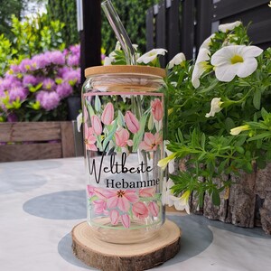 May include: A clear glass tumbler with a bamboo lid and a curved glass straw. The glass features a pink tulip floral pattern and the black text "Weltbeste Hebamme" printed in the center. The design is framed by thin pink and green lines.