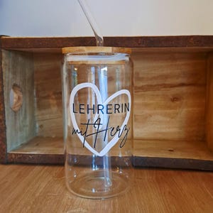 K&ouml;nnte beinhalten: Ein klares Glastrinkglas mit Bambusdeckel und Glasstrohhalm. Auf der Vorderseite befindet sich eine wei&szlig;e Herz-Grafik mit dem schwarzen Schriftzug LEHRERIN mit Herz im Inneren. Das Glas hat eine zylindrische Form mit einem flachen Boden.