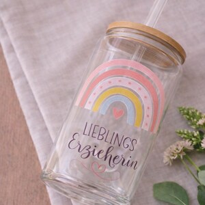 May include: A clear glass tumbler with a bamboo lid and a glass straw. The glass features a colorful rainbow graphic with small stars, a pink heart, and the text "LIEBLINGS Erzieherin" written in black, with a small pink heart flourish below.