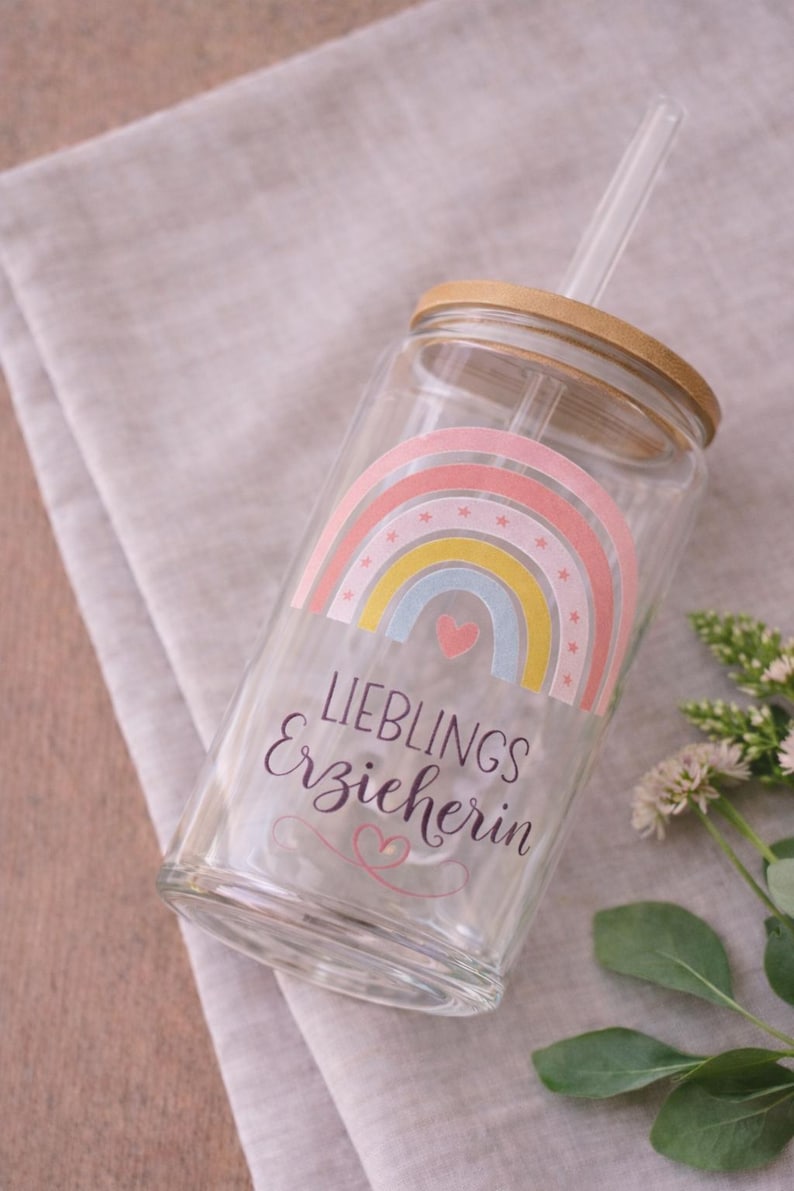 May include: A clear glass tumbler with a bamboo lid and a glass straw. The glass features a colorful rainbow graphic with small stars, a pink heart, and the text "LIEBLINGS Erzieherin" written in black, with a small pink heart flourish below.