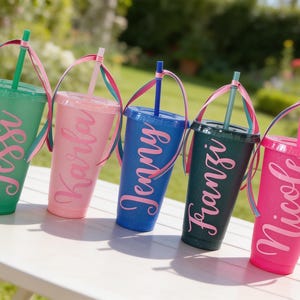 Puede incluir: Cinco vasos de pl&aacute;stico con purpurina, tapas y pajitas, cada uno con un nombre personalizado en letra cursiva. Los vasos son verde, rosa claro, azul, azul verdoso oscuro y rosa intenso, decorados con una cinta de colores en la pajita.