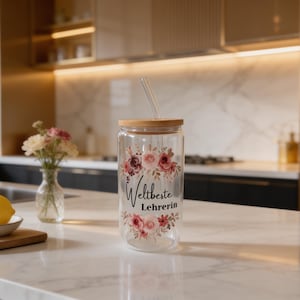 K&ouml;nnte beinhalten: Ein klares Glastrinkglas mit Bambusdeckel und Glasstrohhalm, verziert mit einem Blumenmuster aus rosa und burgunderroten Rosen sowie dem schwarzen Schriftzug "Weltbeste Lehrerin" auf der Vorderseite. Das Glas hat eine zylindrische Form.