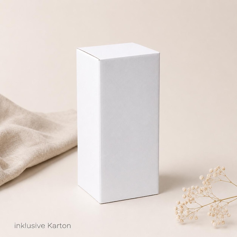 May include: A plain white rectangular cardboard box standing upright. The box has a smooth, matte finish and clean, sharp edges. The text "inklusive Karton" is printed in small, dark gray sans-serif letters at the bottom left of the image.