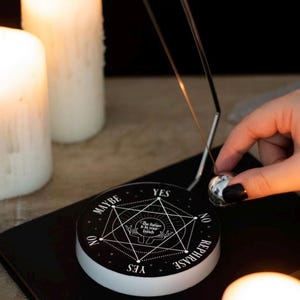 Könnte beinhalten: Ein schwarz-weißes, kreisförmiges Entscheidungs-Pendelgerät mit einem geometrischen Sternmuster, dem Text "The future is in your hands" und den Wörtern "YES", "NO", "MAYBE" und "REPHRASE", die um den Rand einer flachen Basis gedruckt sind.