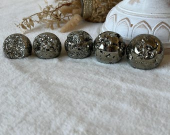 May include: Five metallic pyrite spheres arranged in a horizontal row. Each sphere features a dark, reflective, and textured surface with crystalline clusters. The stones exhibit a natural, uneven, and mineralized appearance with varying shades of silver and gray.