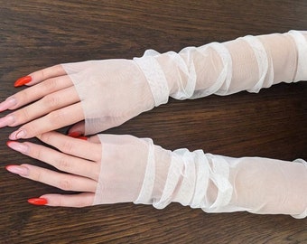 Könnte beinhalten: Ein Paar weiße, fingerlose Handschuhe aus durchsichtigem Stoff mit gerafftem, gekräuseltem Design. Die Handschuhe sind aus einem zarten, leichten Stoff gefertigt.