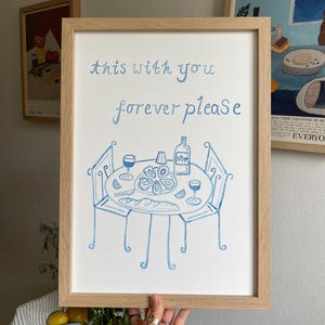 May include: A white ceramic mug with a black handle and the text "But First, Coffee" in a bold, black font. The mug is on a wooden surface. The mug is approximately 10 cm tall.