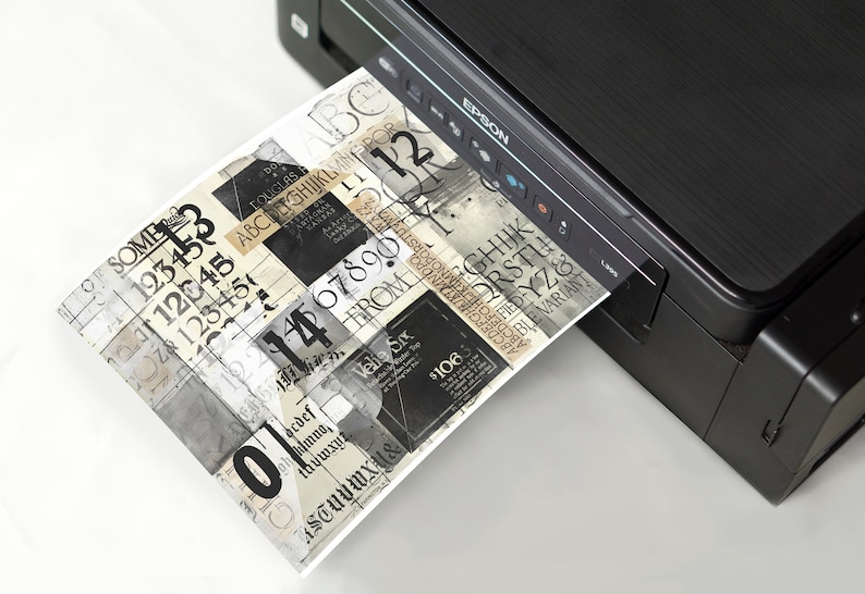 May include: A black and silver printer with a sheet of paper coming out of the paper tray. The paper has a collage of black and white text and numbers.