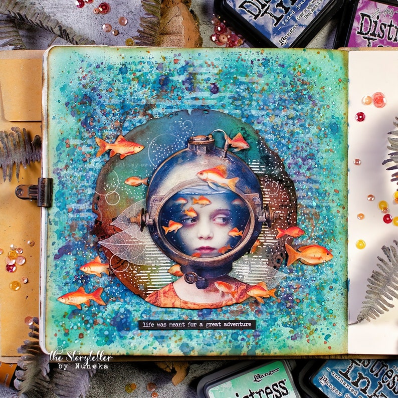 May include: A mixed media art journal page with a blue, green, and white background. The page features a child's face inside a vintage diving helmet with gold fish swimming around it. The text "life was meant for a great adventure" is printed at the bottom of the page.