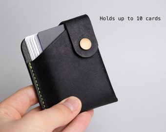 May include: Black leather card holder with a brass button closure. The card holder is stitched with green thread and holds up to 10 cards. The card holder is held in a hand.