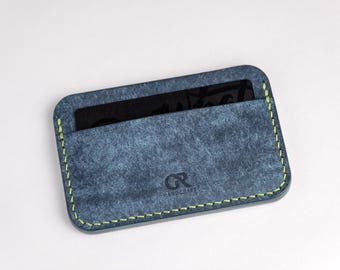 May include: A blue leather card holder with a green stitch detail. The card holder has a single card slot and the text "GR HANDCRAFT" is embossed on the front.