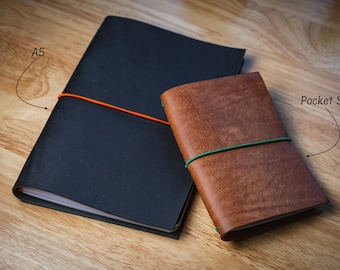 May include: Two leather-bound notebooks, one black and one brown, with elastic bands. The larger notebook is labeled "A5" and the smaller notebook is labeled "Pocket Size".