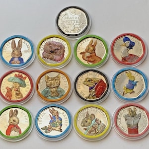 May include: A collection of twelve heptagonal coins featuring colorful illustrations of Beatrix Potter characters, including Peter Rabbit, Jemima Puddle-Duck, and Mr. Jeremy Fisher. Each coin is encased in a clear protective plastic capsule.