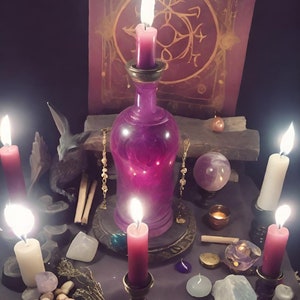 May include: A mystical scene featuring a purple bottle with a lit candle, surrounded by other candles, crystals, and a book. The candles are in various holders, and the scene is set on a dark surface, creating a magical ambiance.