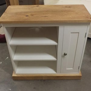 May include: White wooden cabinet with a single door and two shelves. The cabinet has a natural wood top and a base.