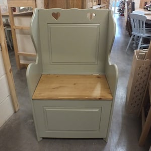 May include: A light green wooden bench with a hinged seat and storage space. The bench has a high back with heart-shaped cutouts and a light wood top.