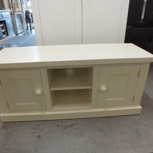 May include: White wooden TV stand with two doors and a shelf. The stand has a simple design with rounded edges.