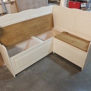 May include: White corner bench with a wooden seat and storage compartments. The bench has a curved back and is made of wood.