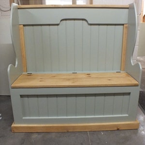May include: A wooden storage bench with a high back and a lift-up seat. The bench is painted in a light blue-grey colour, with natural wood accents on the seat and trim. The bench is approximately 122 cm wide.