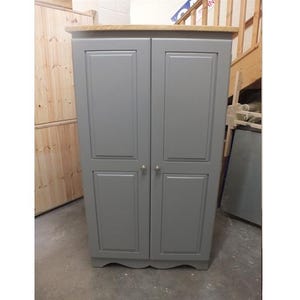 May include: A grey wooden double-door cabinet with a light wood top. The cabinet has a simple design with two panels on each door.
