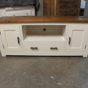 May include: White wooden TV stand with two doors, a drawer, and an open shelf. The stand has a natural wood top and black metal handles.