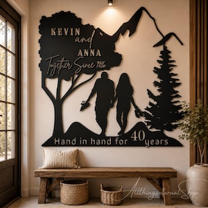 May include: A large black wall-mounted sign featuring a silhouette of a couple walking between a tree and a pine forest with mountain peaks. The text reads KEVIN and ANNA, Together Since 1986, and Hand in hand for 40 years in raised lettering.