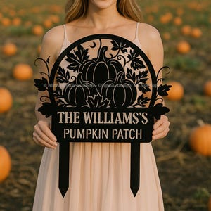 May include: Black metal pumpkin patch sign with a decorative pumpkin and leaf design. The sign reads "THE WILLIAMS'S PUMPKIN PATCH". The sign is held in front of a field of pumpkins.