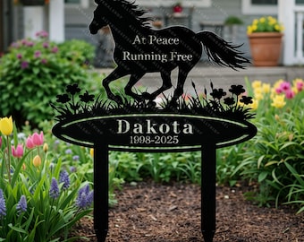 Può includere: Paletto da giardino in metallo nero con la silhouette di un cavallo che corre, il nome "Dakota" e le date "1998-2025". Il testo "At Peace Running Free" è sopra il cavallo. Il paletto è circondato da erba e fiori stilizzati.