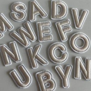 May include: A set of white felt letters with a beige outline. The letters are arranged in a random order and include the letters M, S, A, D, V, W, E, F, O, N, K, C, U, B, Y, and N.
