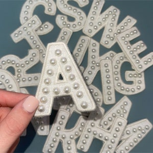 May include: A set of white pearl-embellished felt letters, including the letters A, S, W, E, R, T, Y, U, I, O, P, and G. The letters are arranged in a random pattern.