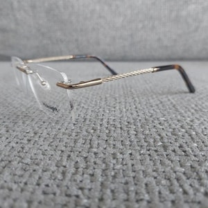 Op de afbeelding: Bril zonder montuur met goudkleurige metalen montuur en veren. De veren hebben een gedraaid ontwerp en gaan over in een donkerbruine kleur bij de oren. De glazen zijn helder.