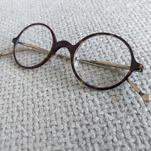 Może przedstawiać: Okulary okrągłe w kolorze żółwim z srebrnymi metalowymi zausznikami.