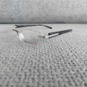 Puede incluir: Un par de gafas negras y plateadas con lentes transparentes. El nombre de la marca "TAG Heuer" es visible en la montura.