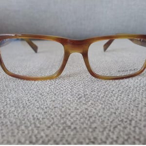 May include: Brown tortoise shell eyeglasses with clear lenses. The brand name "alain mikli" is printed on the right lens.