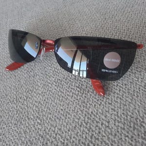 May include: Red and black sunglasses with mirrored lenses. The sunglasses have a label that says "Ideal Image 100% UV 400+"